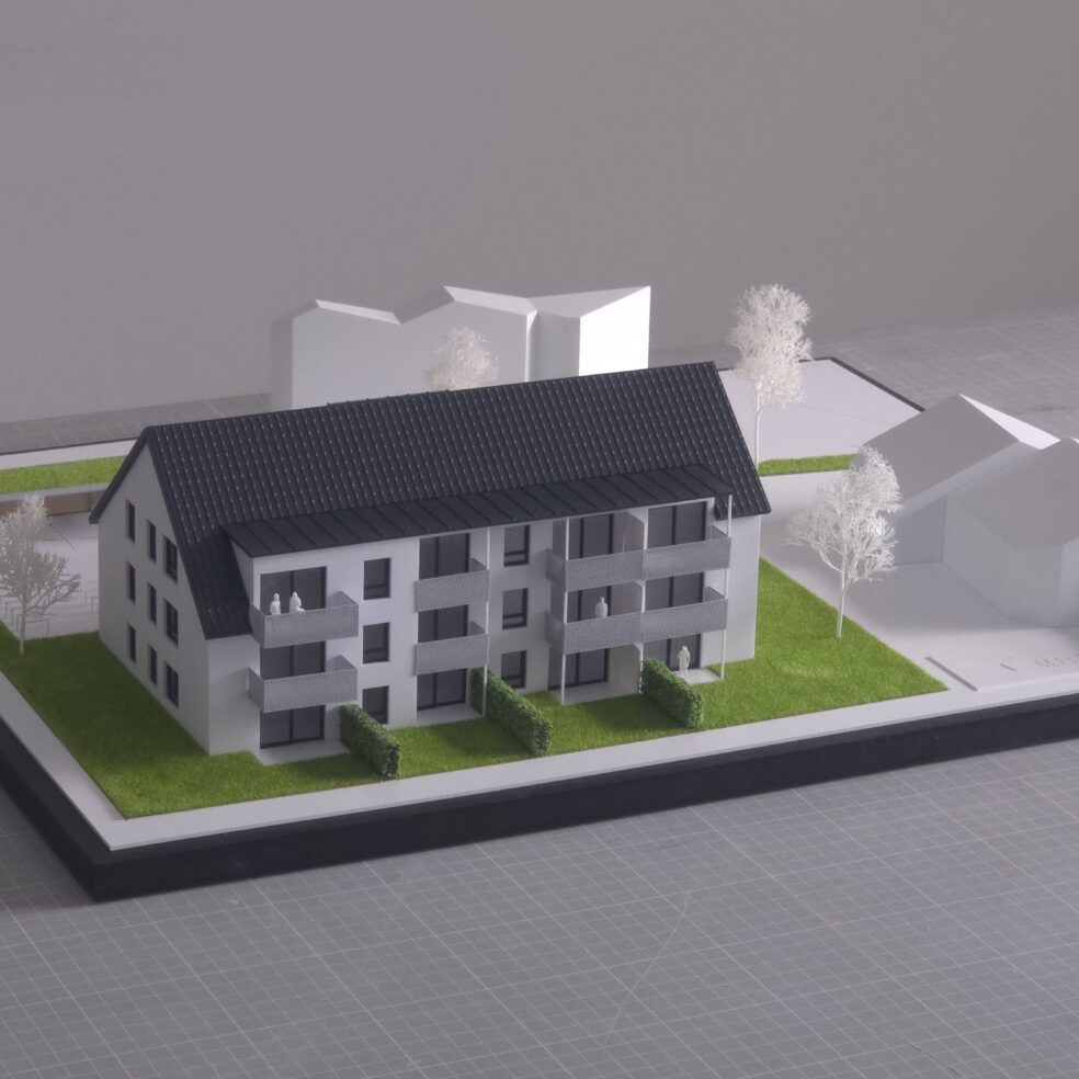 Präsentationsmodell eines Mehrfamilienhauses im Maßstab 1:100 mit abstrahiertem Umfeld und Grünflächen.