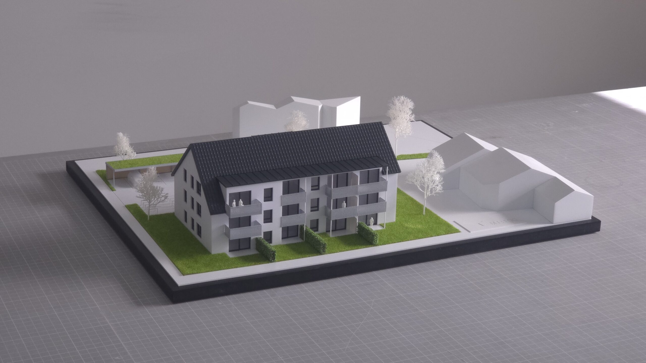 Präsentationsmodell eines Mehrfamilienhauses im Maßstab 1:100 mit abstrahiertem Umfeld und Grünflächen.