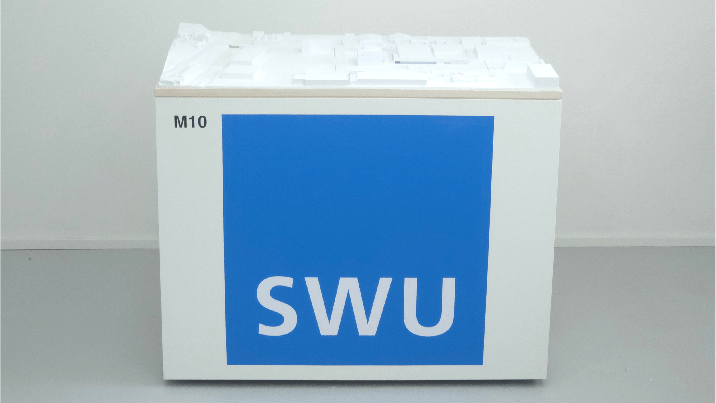 Umgebungsmodell des SWU-Standorts auf einem weißen Ausstellungssockel mit blauem SWU-Logo.